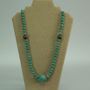 Vintage turquoise bead necklace with central statement stone and accent beads, displayed on neutral fabric bust